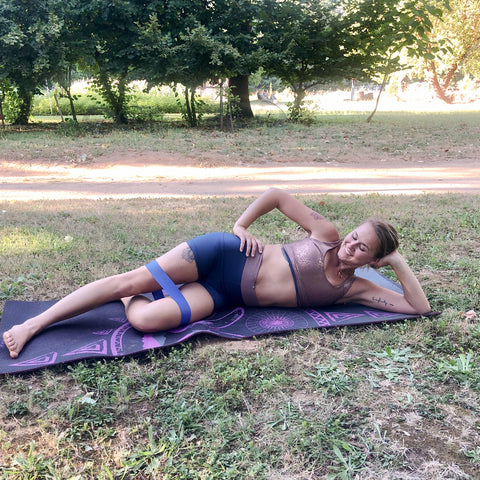 A woman is lying on her side with a resistance band around her thighs about to perform a leg lift exercise.