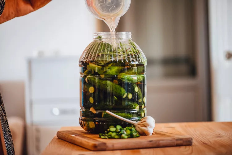 Woman Pouring Water into Jar of Pickles