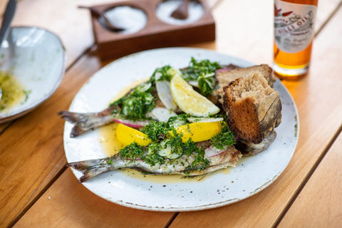 Plato de pescado asado con limón, verduras y pan.