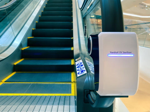 UV light device is attached to an escalator handrail at a shopping mall to disinfect, sanitize, and sterilize the surface from germs, pathogen, viruses, and bacteria 