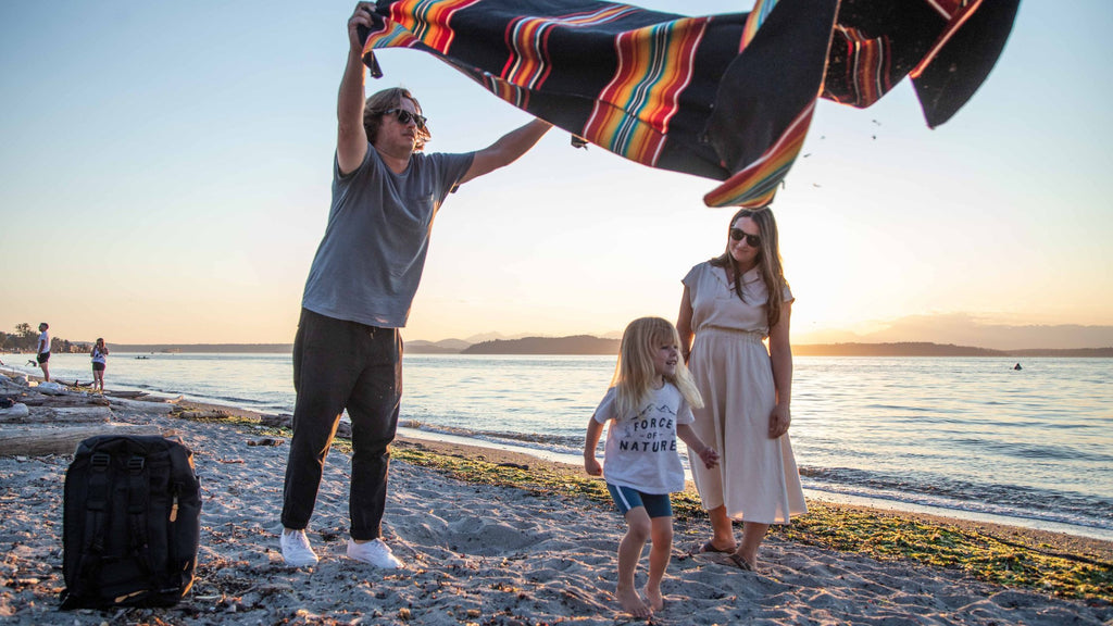 family prepares for a picnic at the beach, diaper bag in right corner