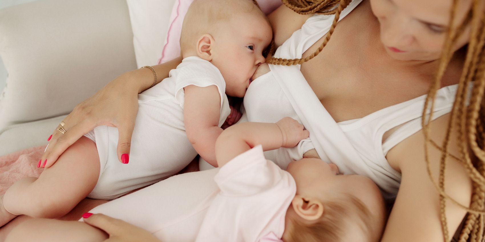 Mother breastfeeding twin newborns while laying on a couch