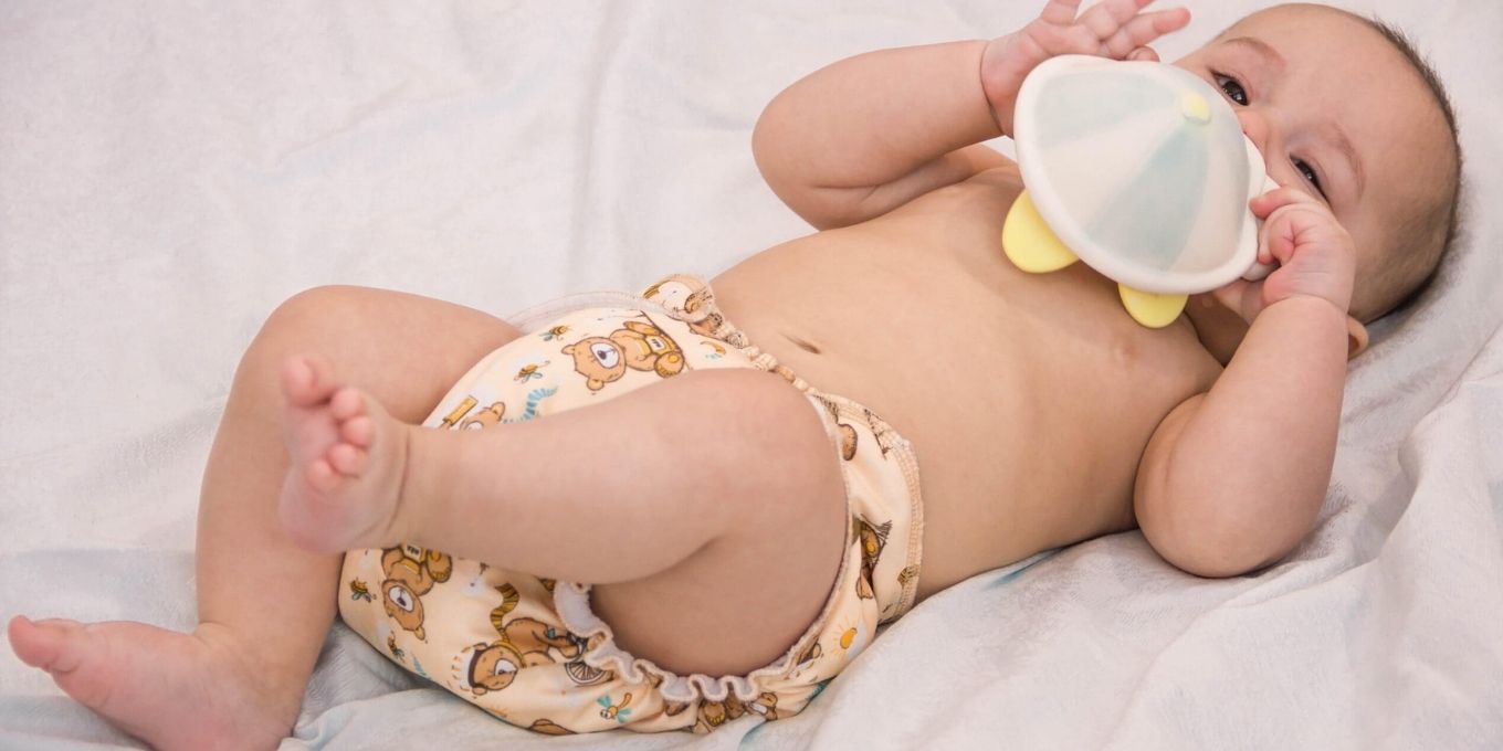 Baby laying on back with disposable diaper on and holding a toy