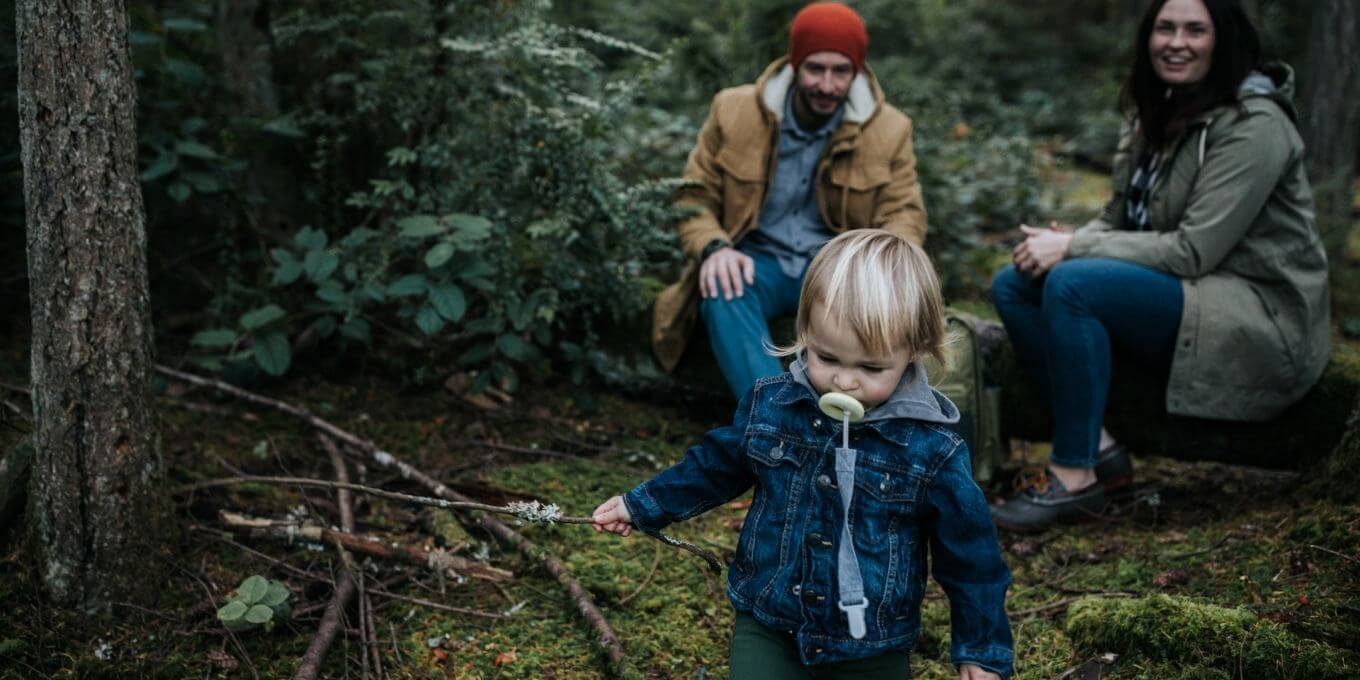 Small child in the forest with parents watching in the background