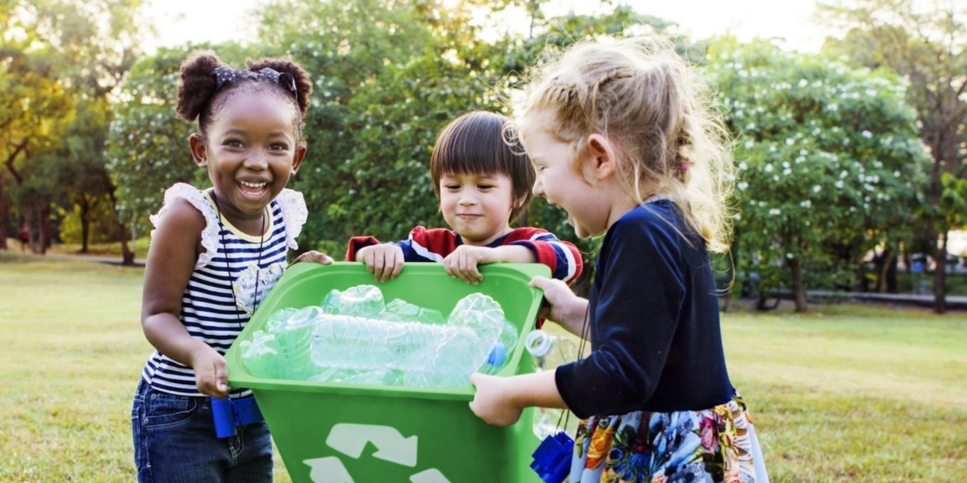 Three children carrying a green recycle bin together
