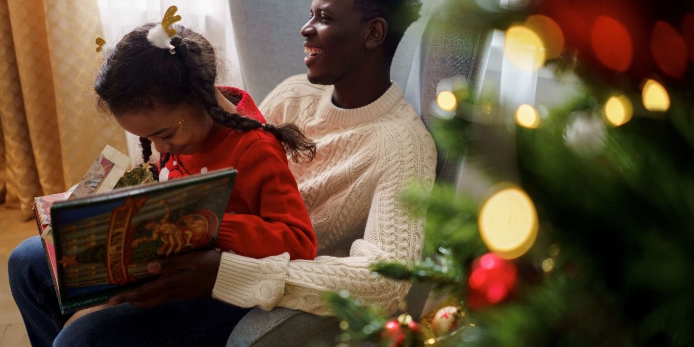 Father holding child on his lap while they read a Christmas book