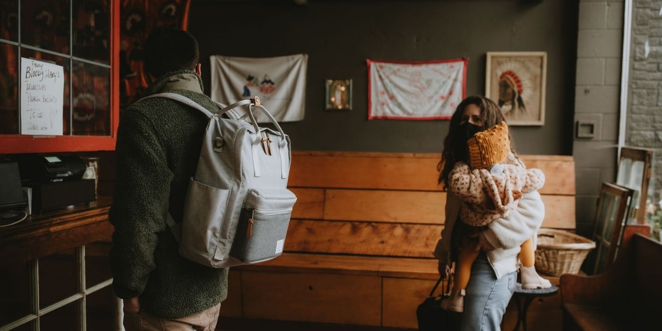 Man standing in line carrying a Heather Grey Elkin Diaper Bag Backpack at a coffee shop with wife and toddler standing behind him