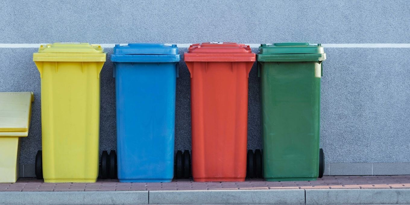 Multi colored garbage bins lined up against a wall