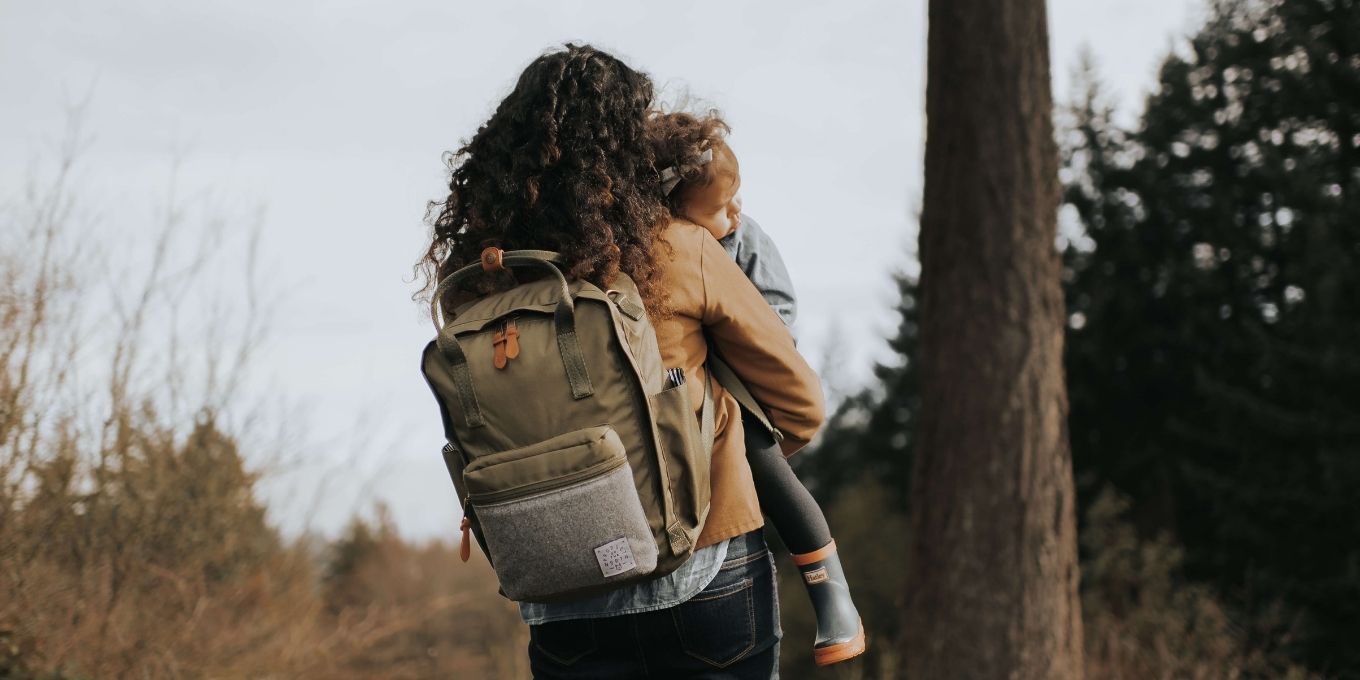Mother holding toddler while carrying Olive Elkin Diaper Bag Backpack