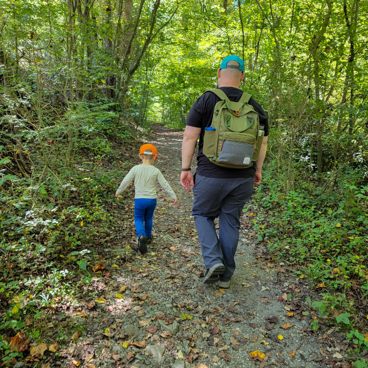 Father and son hiking in the woods.  Dad is wearing a sustainable Olive Elkin Diaper Bag