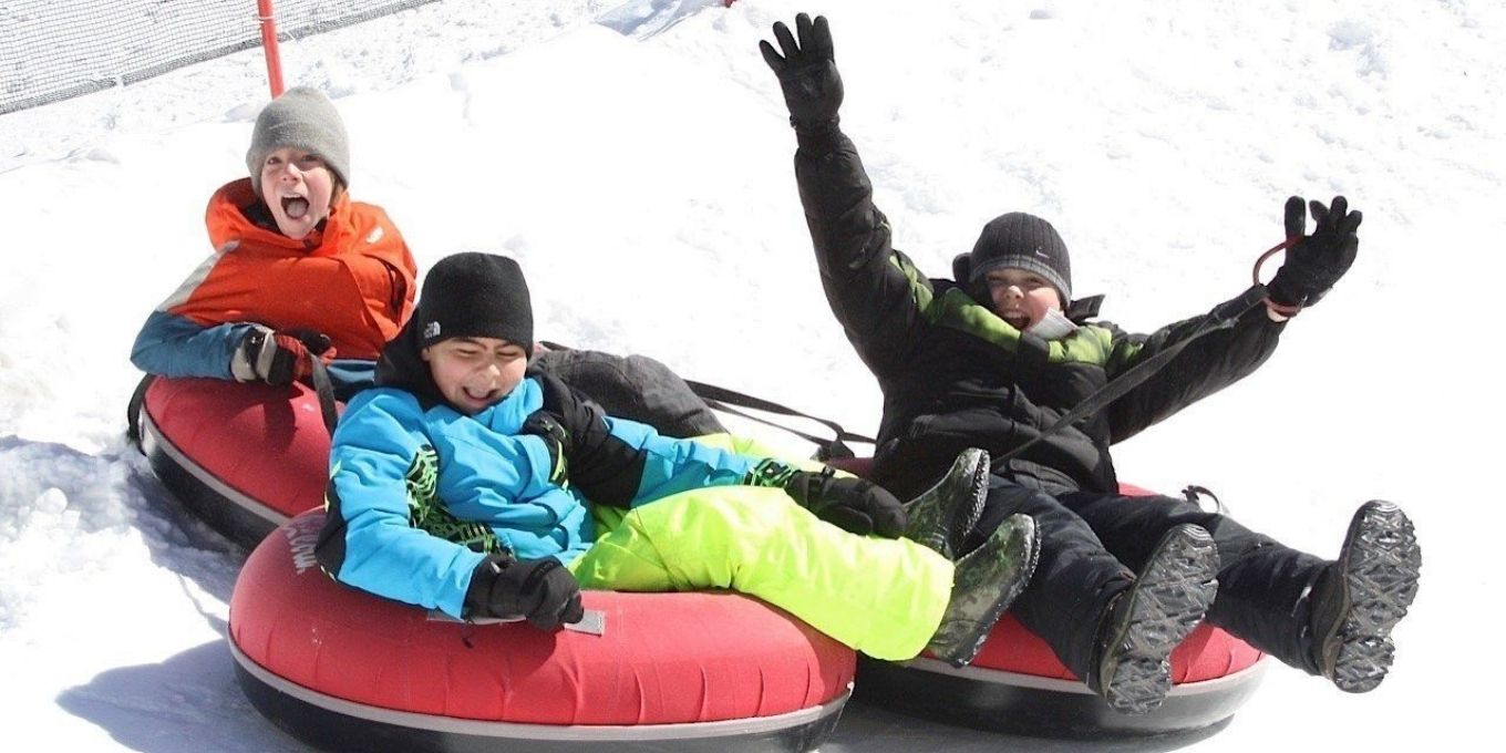 Three young boys sitting in snow tubes in brightly colored clothing