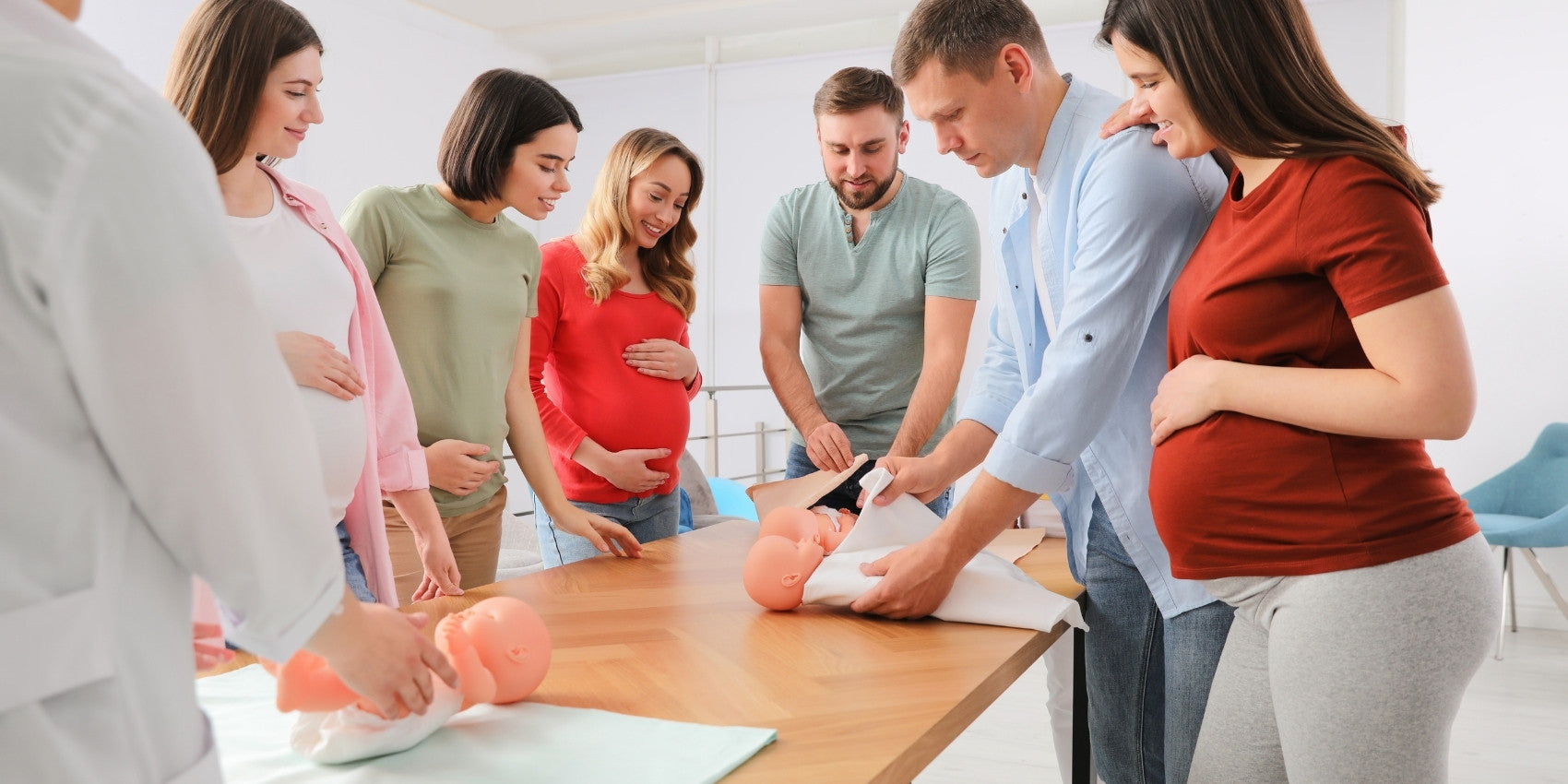 Group of expecting moms and dads wrapping baby dolls in swaddle blankets while taking a class about how to swaddle a baby