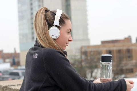 Woman wearing headphones holding  a water bottle with creatine HCl to fuel her run.
