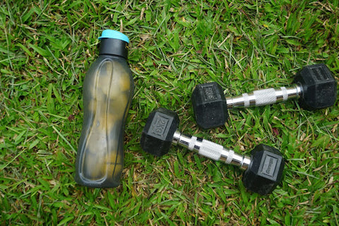 Water bottle with the best creatine HCl in the grass next to a set of two kg dumbbells.