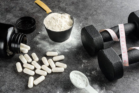 An image of dumbbells wrapped in measuring tape, a bottle of spilled creatine pills, and two creatine powder in different sizes.