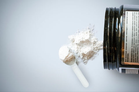 A photo from above a table where a canister of creatine is knocked over and creatine powder is spread across the table along with a measuring cup full of creatine.