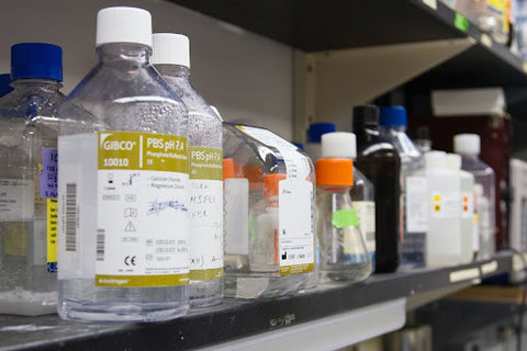 A row of various glass bottles with chemicals inside arranged along a stainless steel shelf.