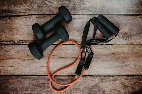 Two small dumbbells and an elastic workout band on a wooden table.