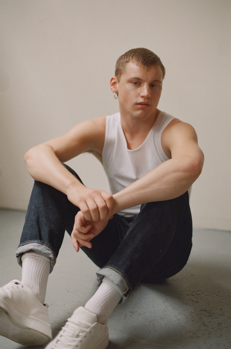 Quinton sitting on floor in jeans and tank top