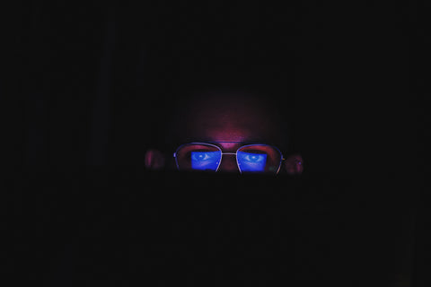 man looking at laptop screen reflecting blue light onto his glasses