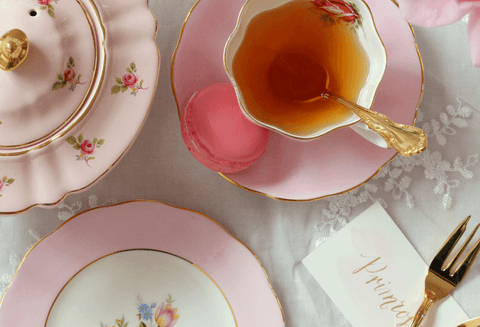 pink tea cup with tea inside, gold cake fork and pink sugar pot