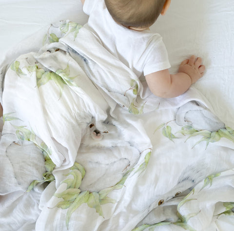 baby in white with a Koala swaddle blanket draped over