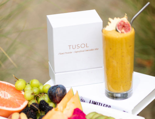 A smoothie glass surrounded by assorted fruits and a product box with the label 'TUSOL'.