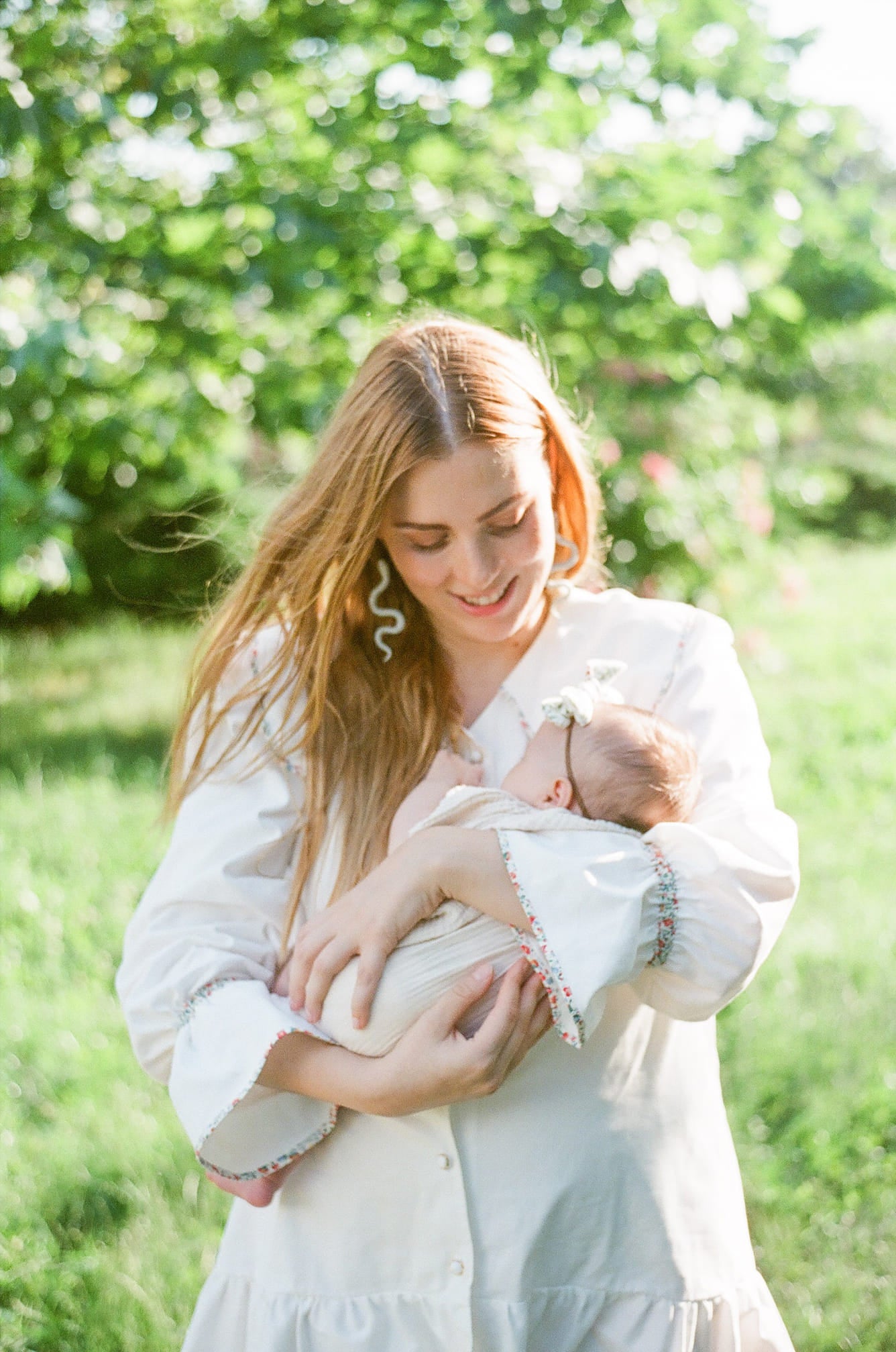 A woman holding a baby in a green field during a maternity photo session, shot on fujifilm 400h real film.