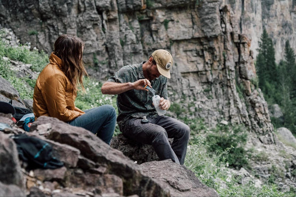 Couple sitting on rock while adding DripDrop ORS to water