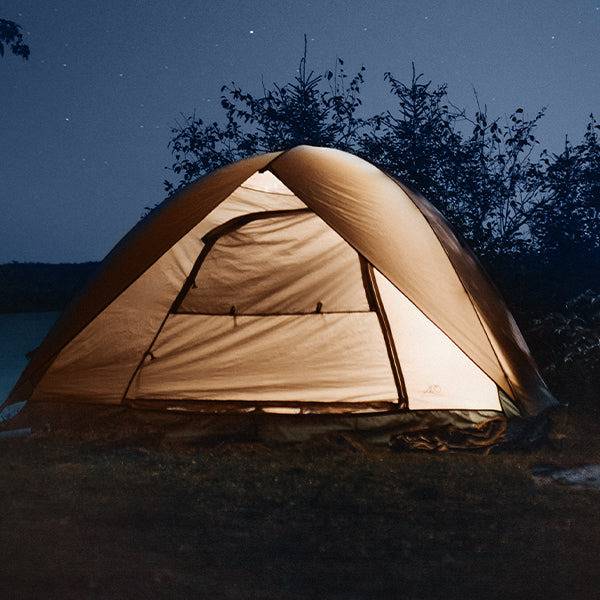camping tent in an outdoor natural area with trees, tent is glowing from inside