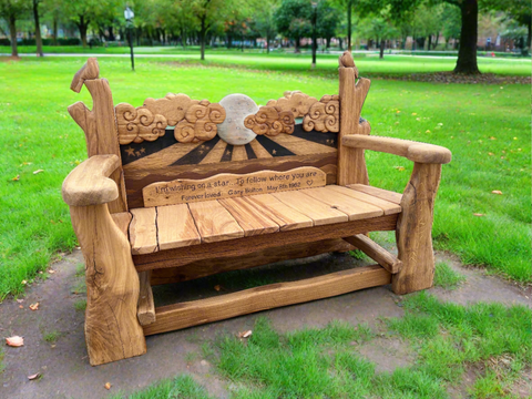 Detailed view of a custom-made wooden bench, highlighting the carved clouds, crescent moon, and birds on the armrests. The backrest features an engraved memorial message, enhancing the bench's sentimental value