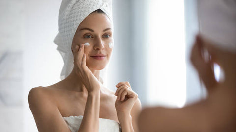 Mujer poniéndose crema en su rostro con toalla en la cabeza
