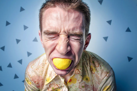 a young adult male with a lemon in his mouth. His face is puckered likely from the sour taste.