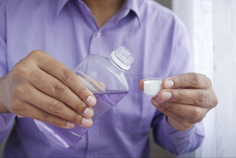 A man holding mouthwash and its cap as if preparing to use it. 