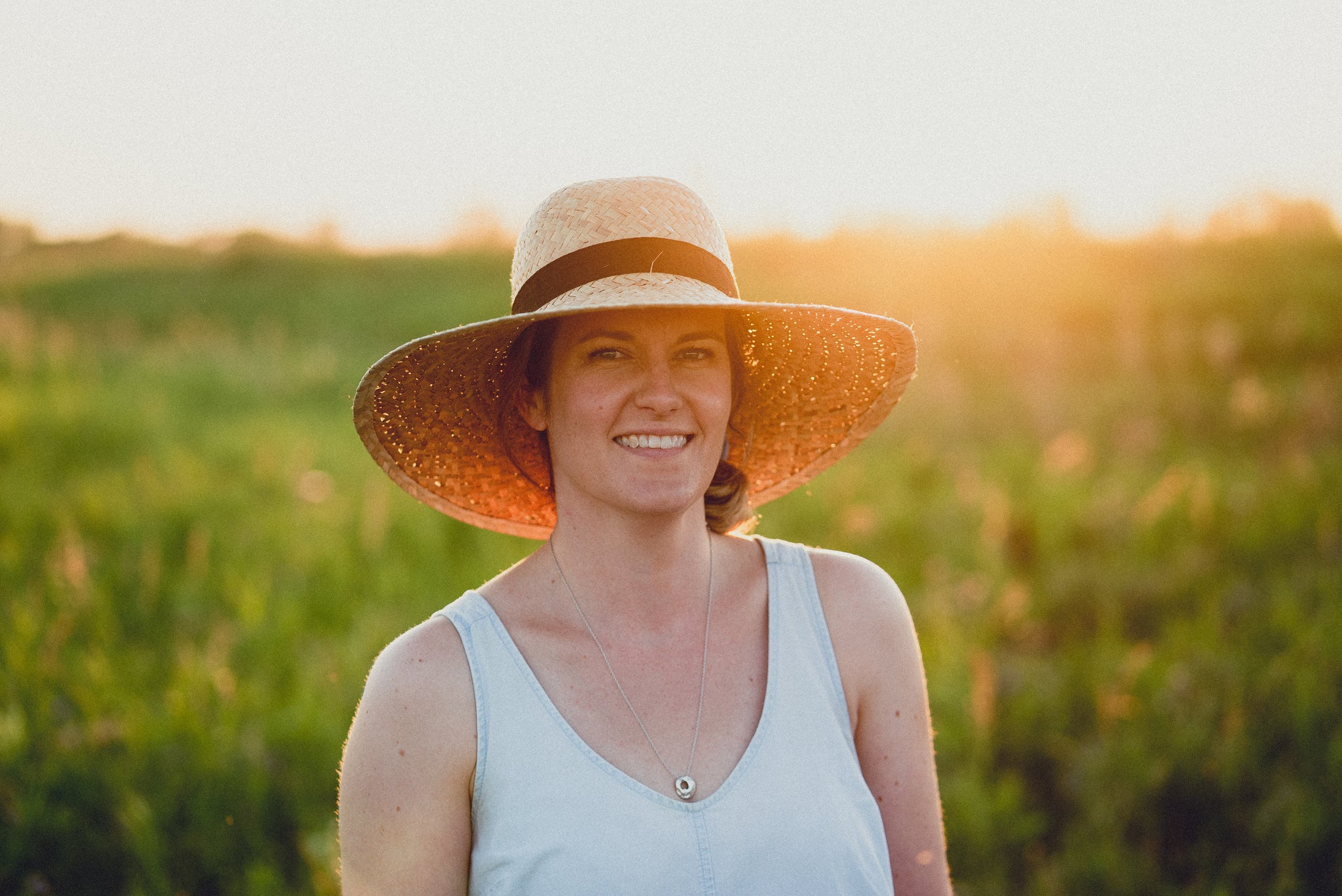 Erin Kembel (owner and designer at EMK Everyday) standing in front of a beautiful prairie sunset wearing a wide brimmed sun hat.