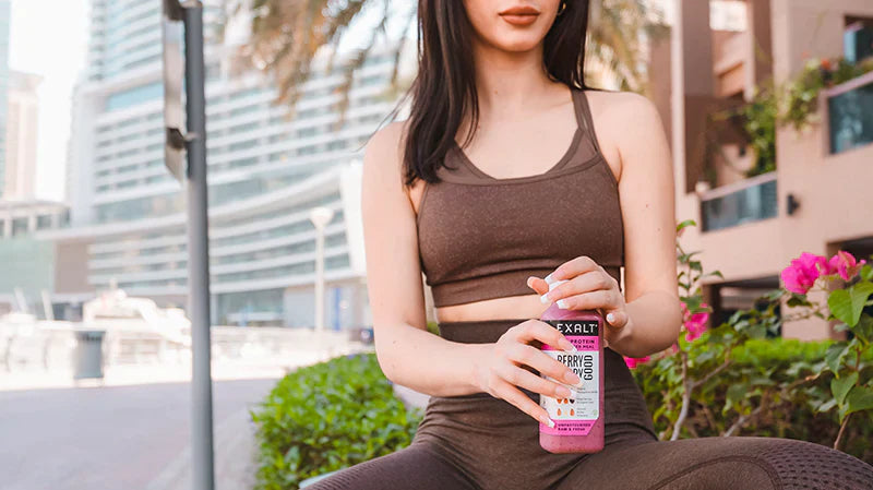 a woman sitting drinking EXALT protein shake