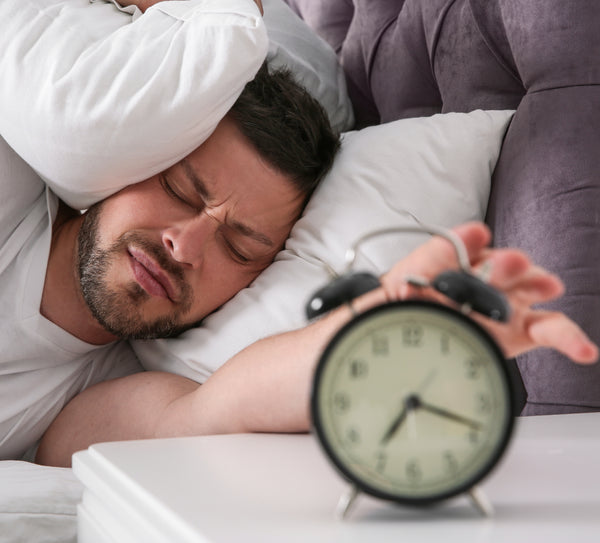 man pressing snooze on his alarm clock