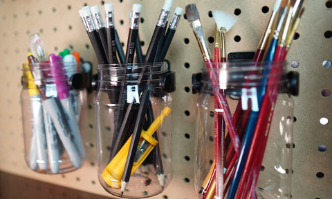 Wallwerx pegboard jars storing art and craft supplies like paint brushes, pencils and pens