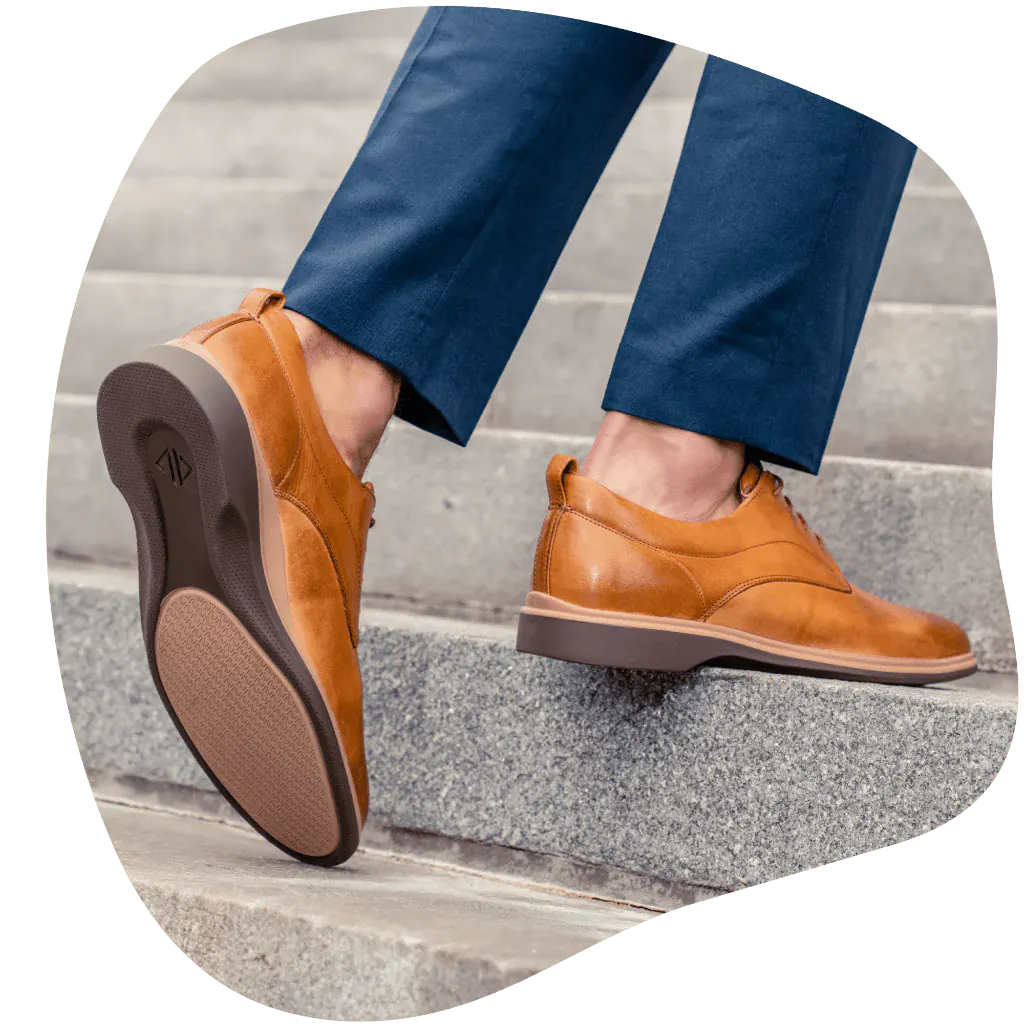  A person walking up steps wearing tan men’s dress shoes with arch support from Amberjack