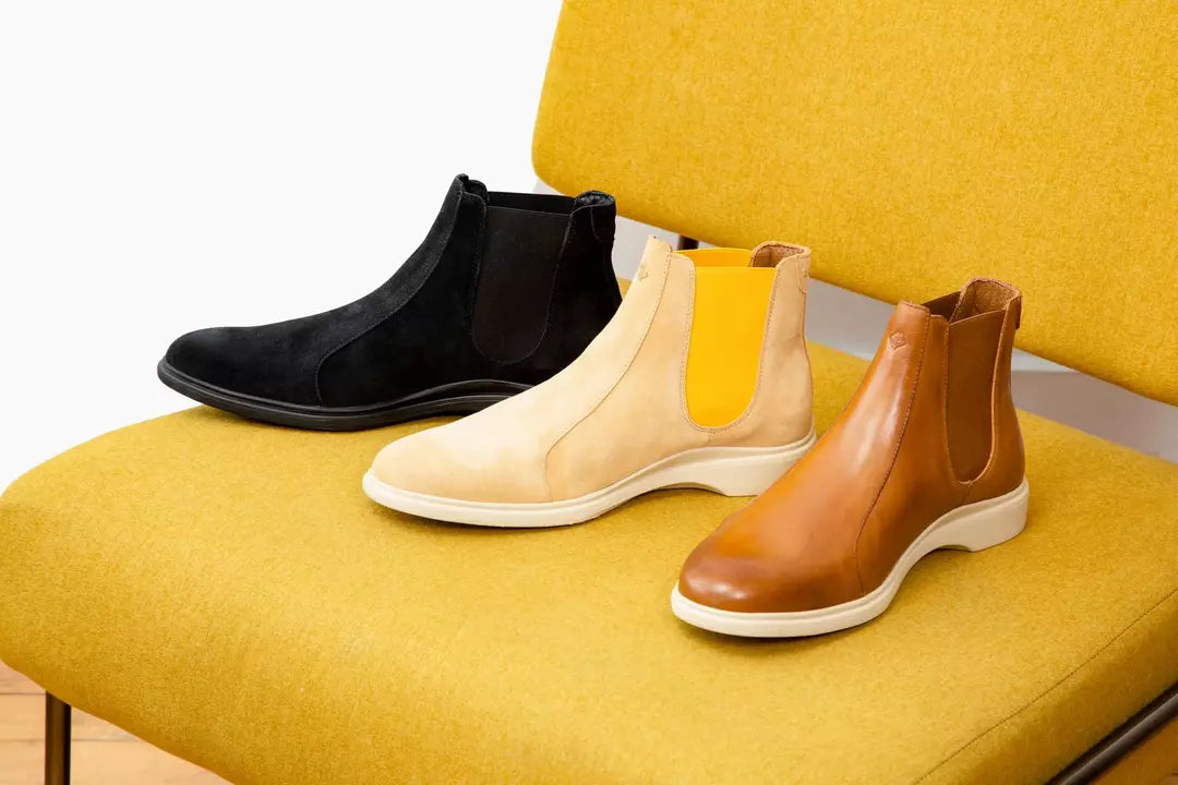 Three distinct Chelsea boots placed on a yellow chair