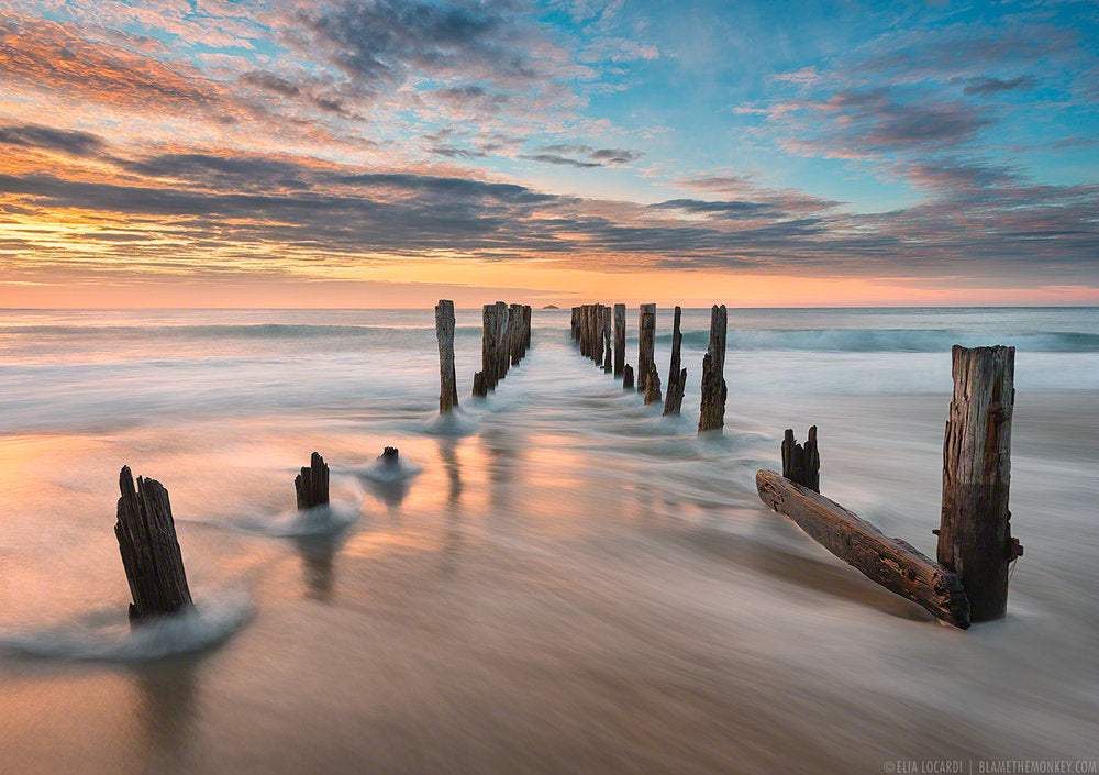 An image at sunset of sea water rushing through the rotted pylons of a collapsed dock