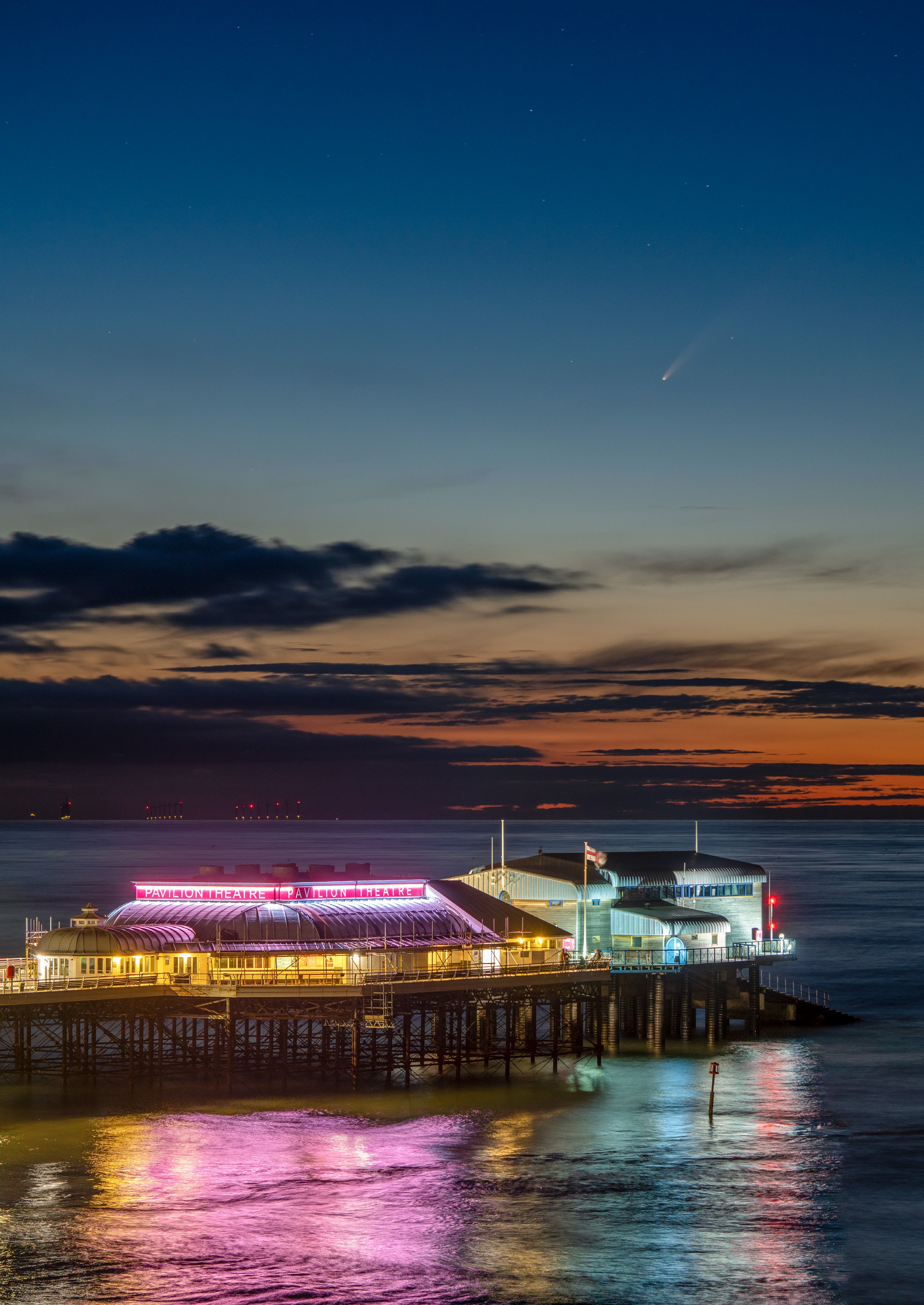 Image of Neowise comet over the Atlantic ocean as seen from Norfolk, UK at dusk with a light up pier in the foreground.