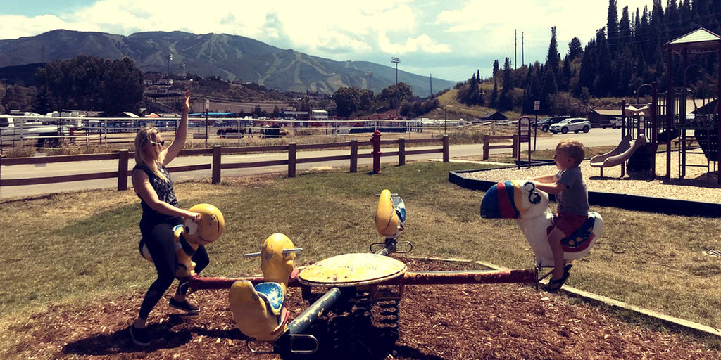 playing on playground in the mountains at a park. mom and baby adventuring outdoors together.