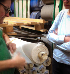 Unsere Schneiderin sichtet mit einer Mitarbeiterin des Stoffproduzenten eine Rolle weißen Baumwollstoff zur Rettung des Materials durch verarbeitung zu Accessoires in unserer Manufaktur.