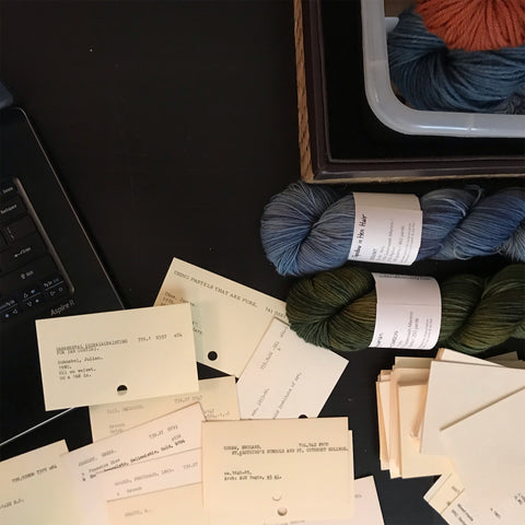A scattered pile of ex-library catalog cards repurposed as Thank You notes, near a laptop and several skeins of hand dyed yarn.