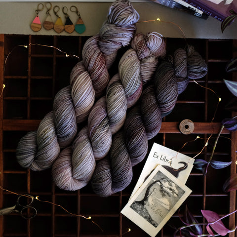 Moody wisteria hues speckled with deep green, rich burgundy, and more grays, near bookplates and the work of Joyce Carol Oates.