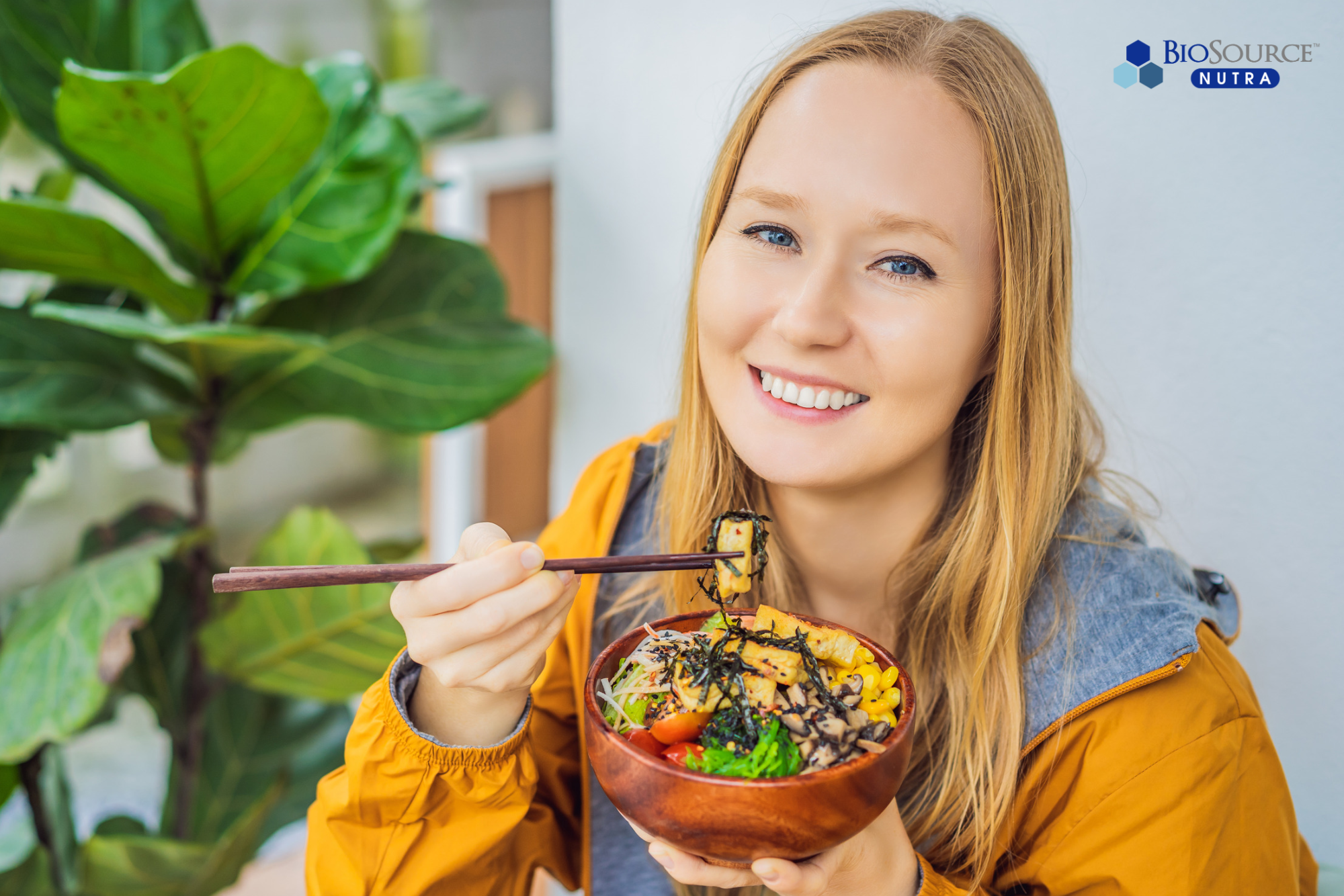 A smiling young woman eats a healthy bowl of food with chopsticks