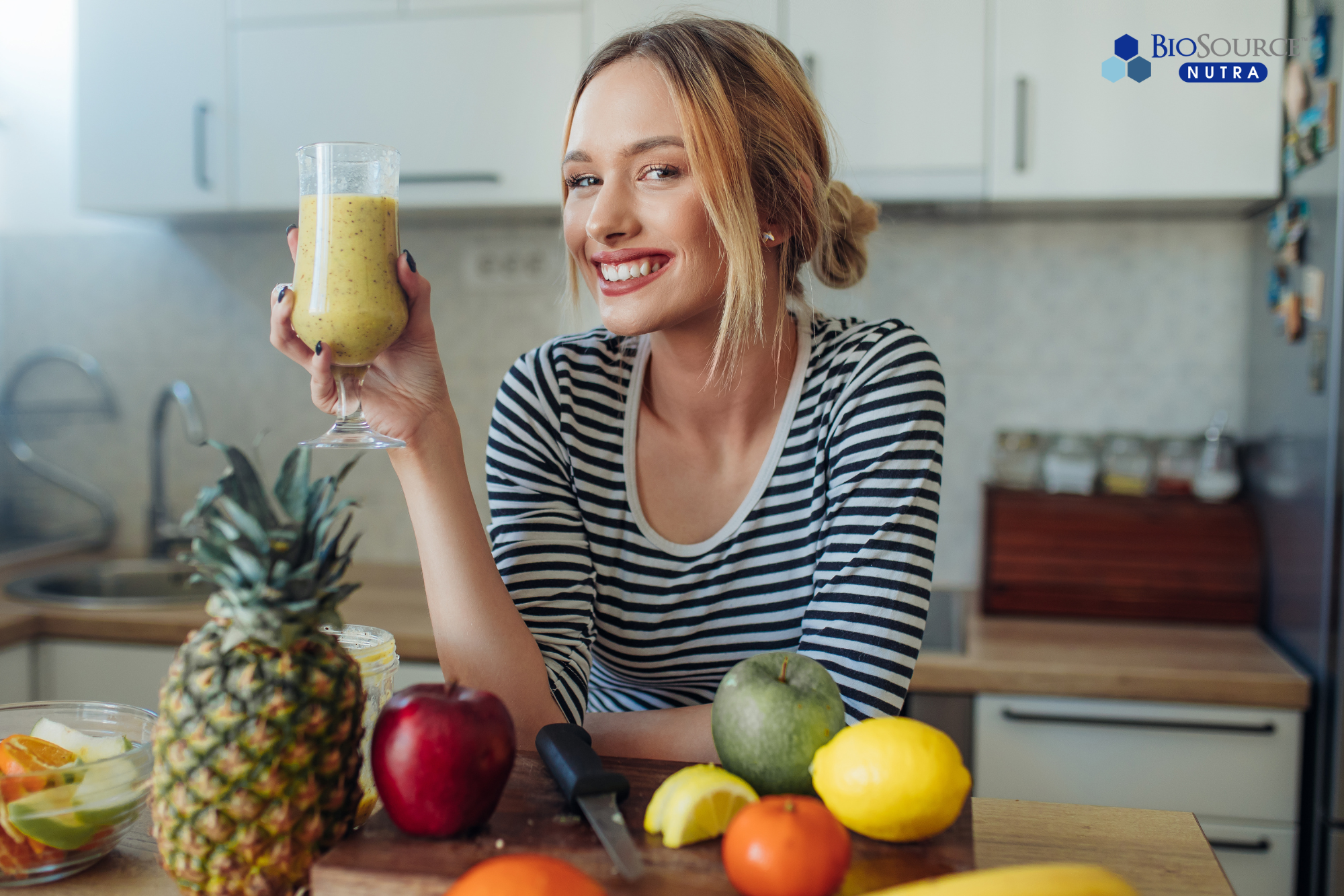 A woman is drinking a yellow smoothie in a kitchen