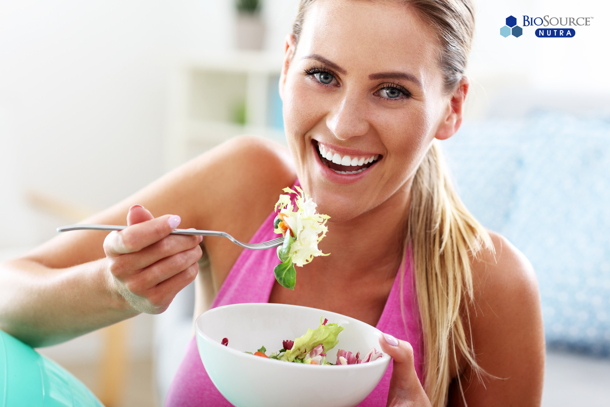 A smiling woman eats a salad