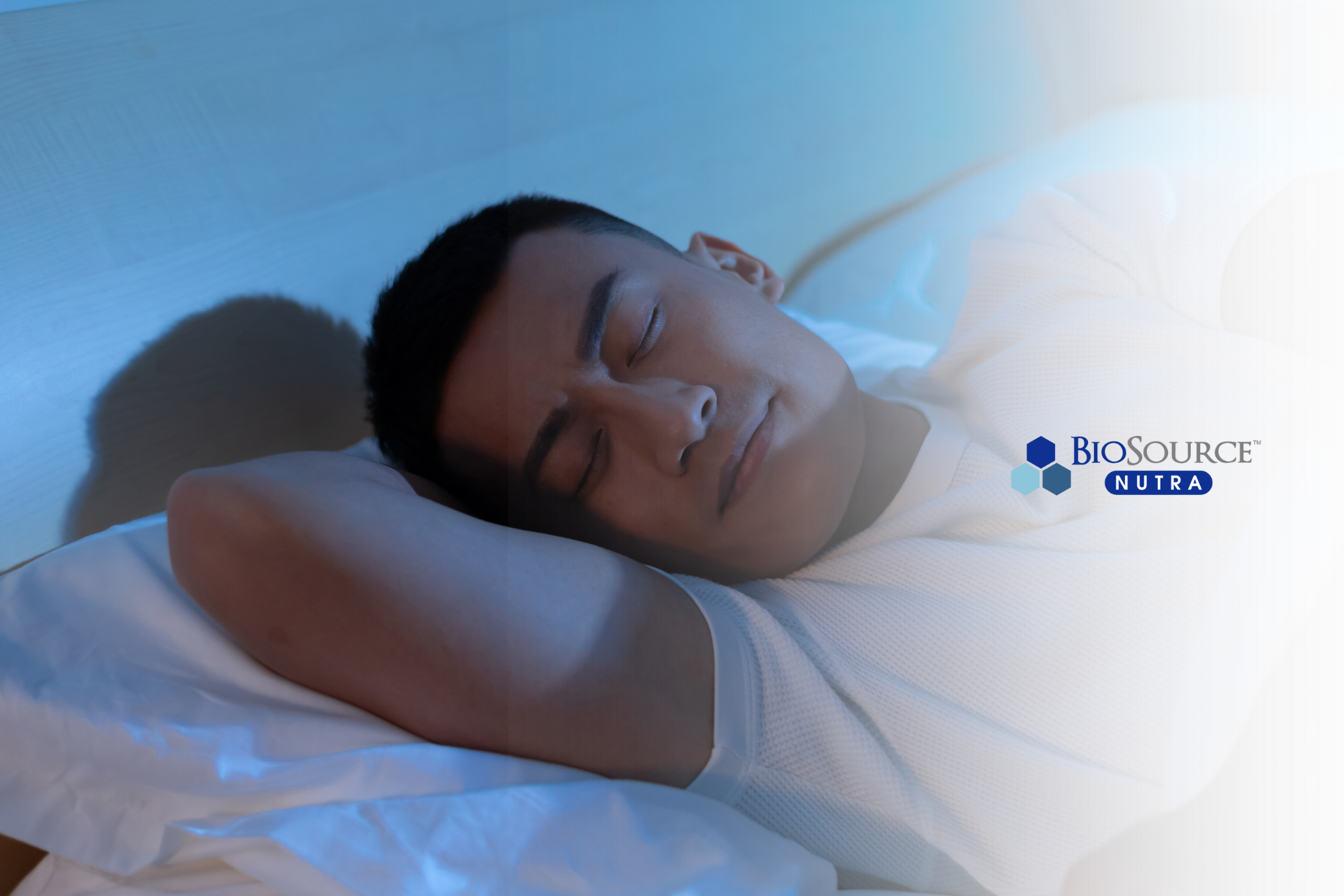 A young man sleeps on white sheets in a cool, dark room